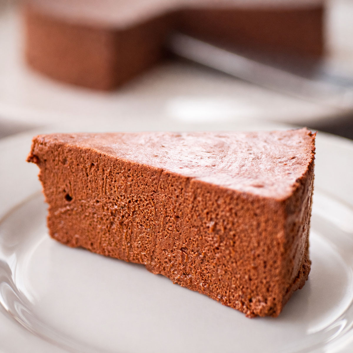 slice of 2 ingredient no bake chocolate banana cake showing the creamy chocolate texture on a white plate with the rest of the cake blurred in the background