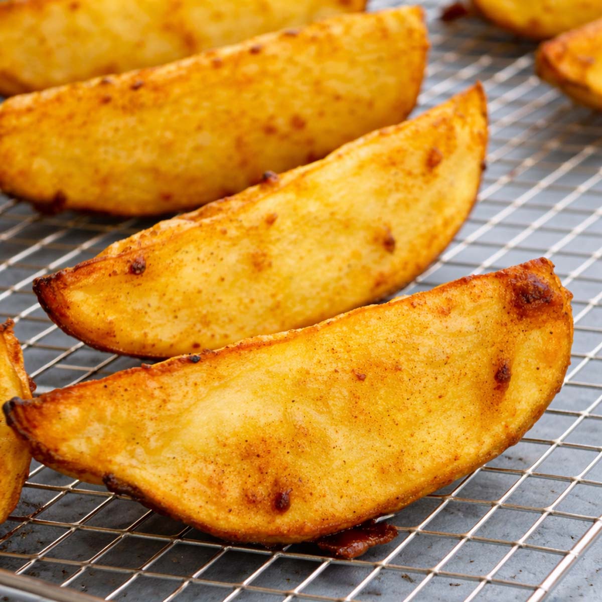 Crispy air fryer potato wedges cooling on a wire rack, golden and seasoned with browned, crunchy edges. 