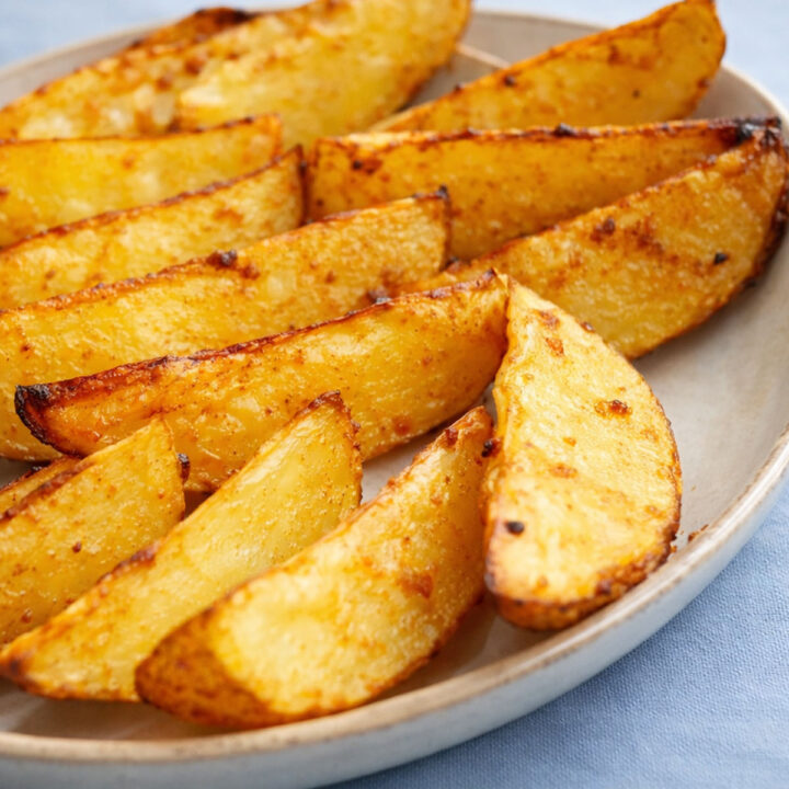 Crispy air fryer potato wedges on a plate, golden and seasoned with browned edges and fluffy centers.