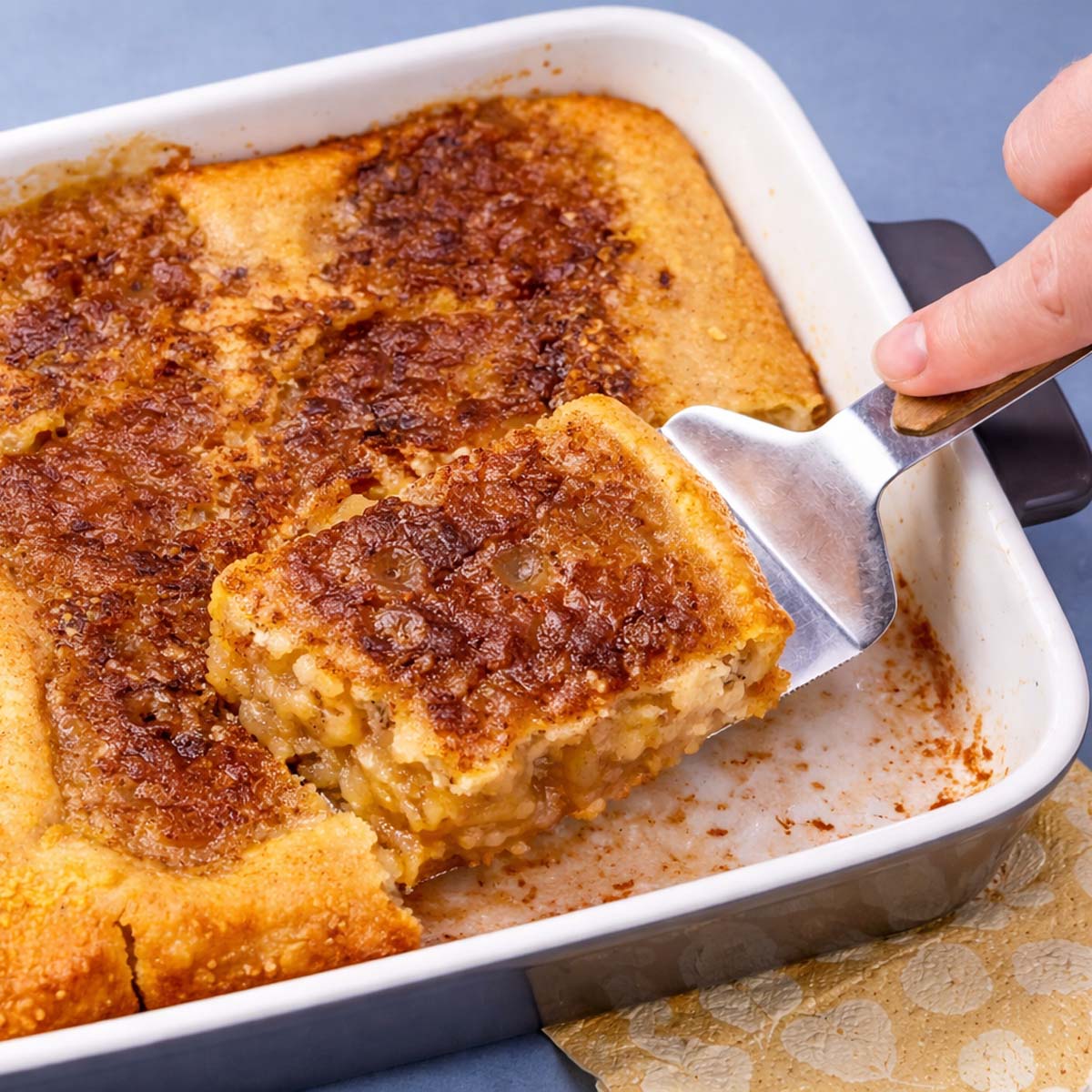 applesauce cobbler in a white baking dish with a slice lifted on a spatula showing the soft apple filling and golden caramelized top