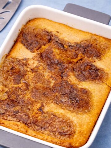 applesauce cobbler in a white baking dish with golden caramelized top on a soft blue background