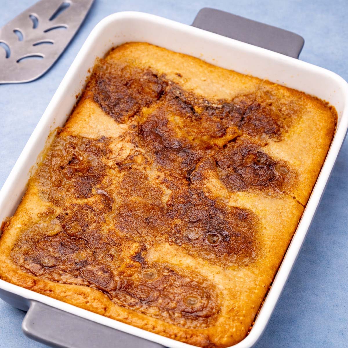applesauce cobbler in a white baking dish with golden caramelized top on a soft blue background