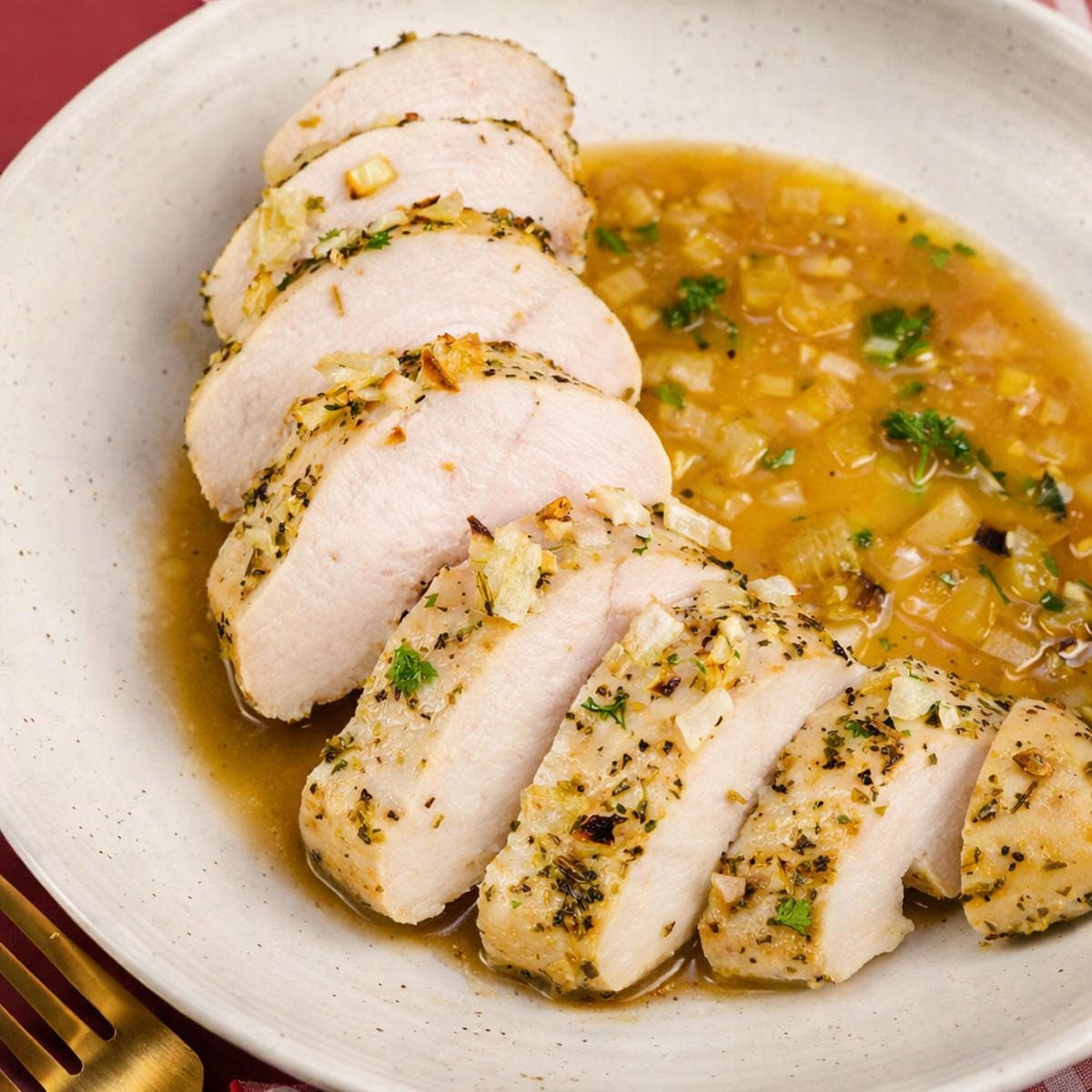 Sliced baked chicken in chicken broth served on a plate with garlic, herbs, and a rich golden onion sauce