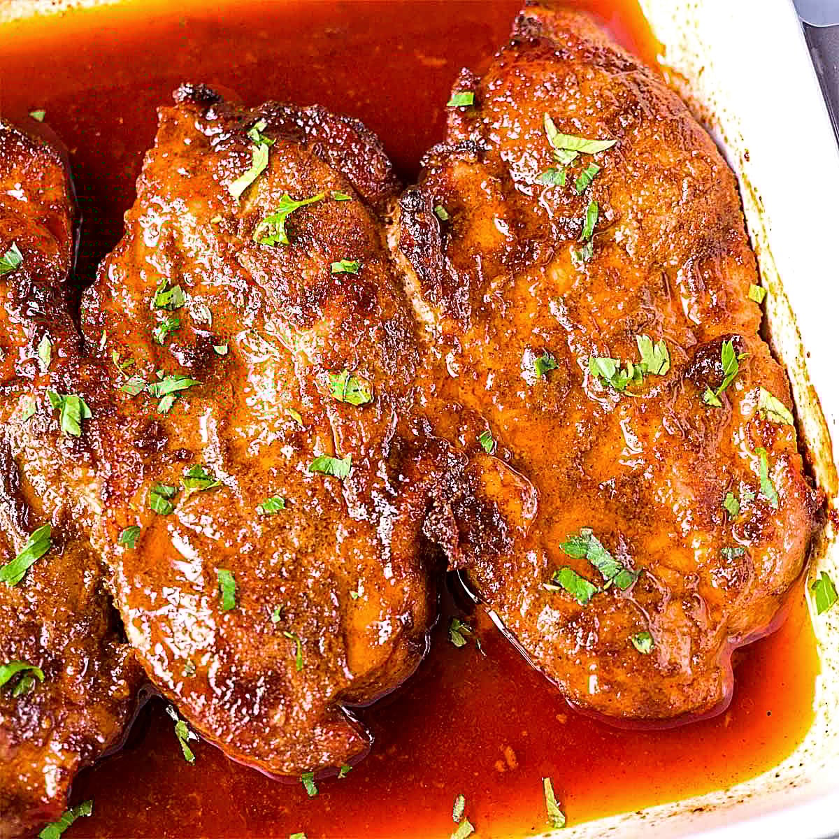 Baked pork steaks in a rich reddish sauce, garnished with chopped parsley and cooked until tender in the oven.