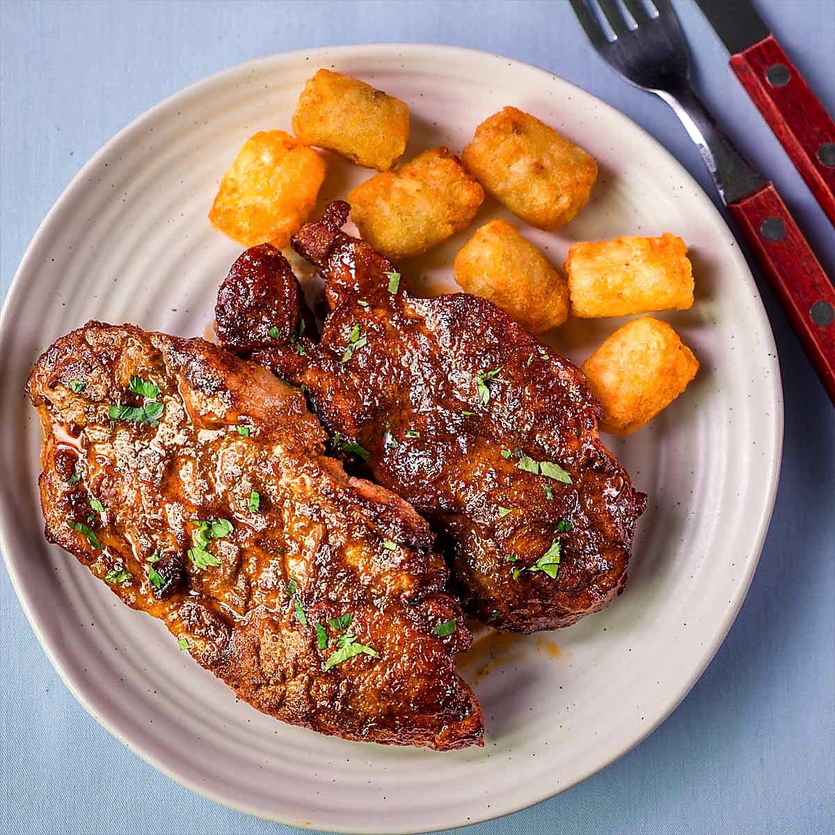 Baked pork steaks served on a plate with crispy potatoes, glazed with sauce and sprinkled with fresh parsley.