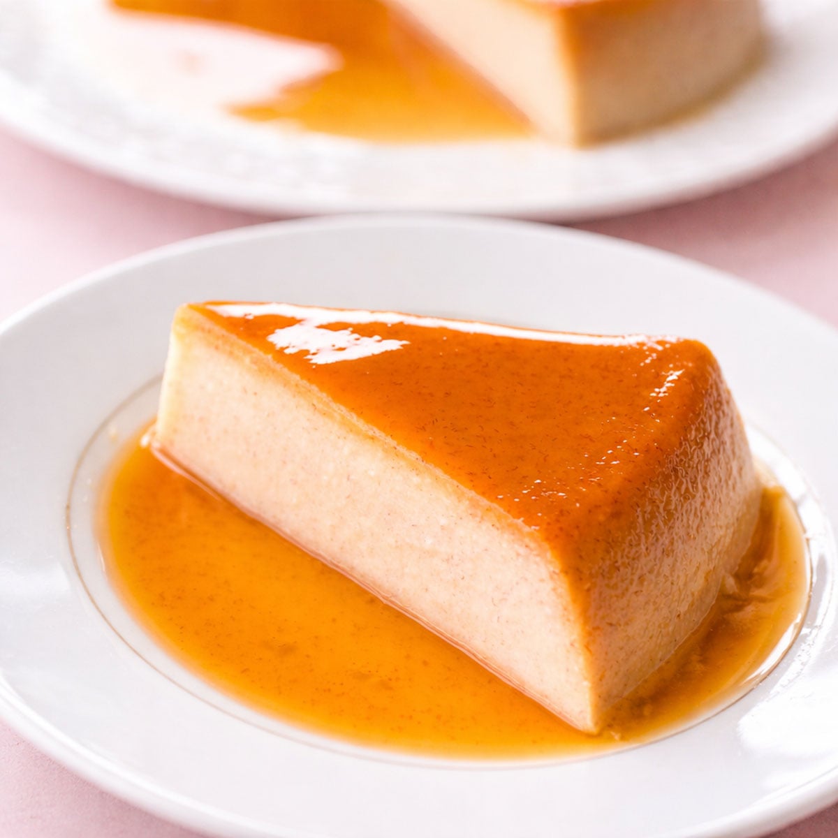 Banana flan slice with glossy caramel sauce on a white plate, creamy custard texture with golden syrup and soft pastel background