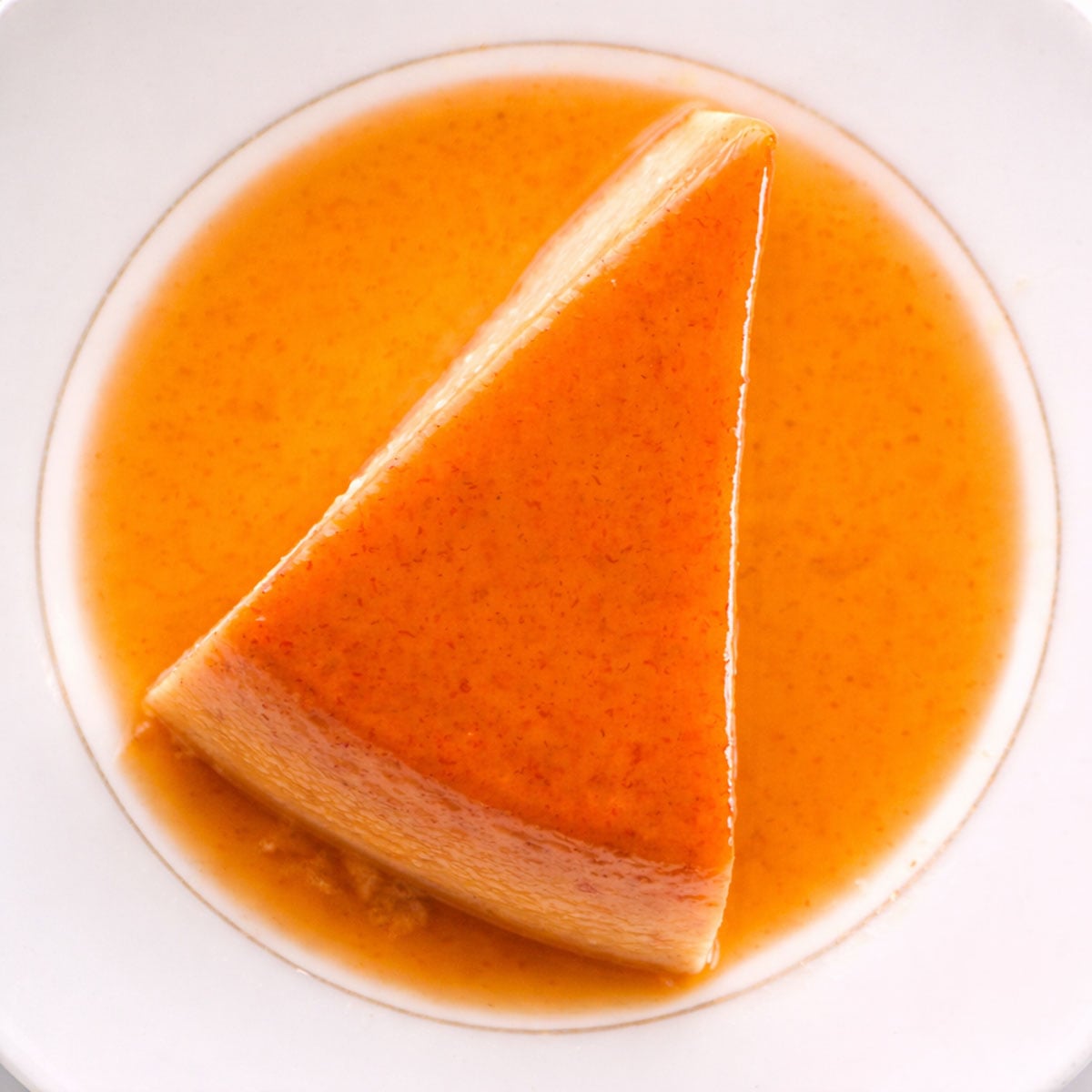 Top view of banana flan slice with glossy caramel topping on a white plate, smooth creamy custard surrounded by golden caramel sauce