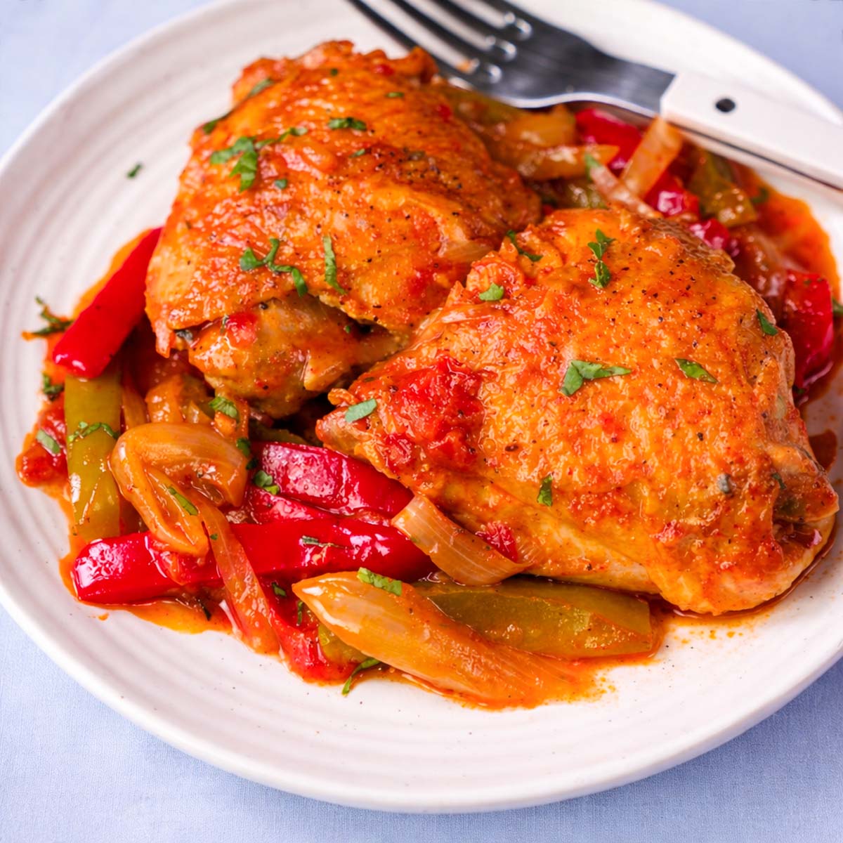 Basque chicken thighs with sautéed red and green peppers and onions in rich tomato sauce on a white plate