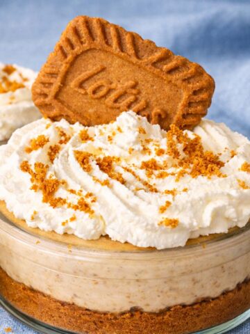No-bake Biscoff cheesecake cups in glass jars with a cookie crumb base, creamy cheesecake layer, whipped topping, Biscoff crumbs, and a Lotus Biscoff cookie on top.