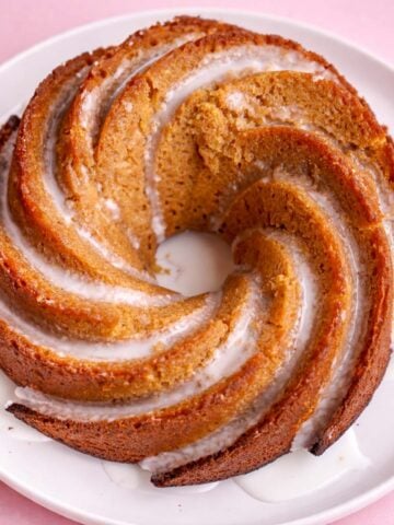 Bishop’s cake with a golden spiral shape and light glaze, served on a white plate against a soft pastel pink background