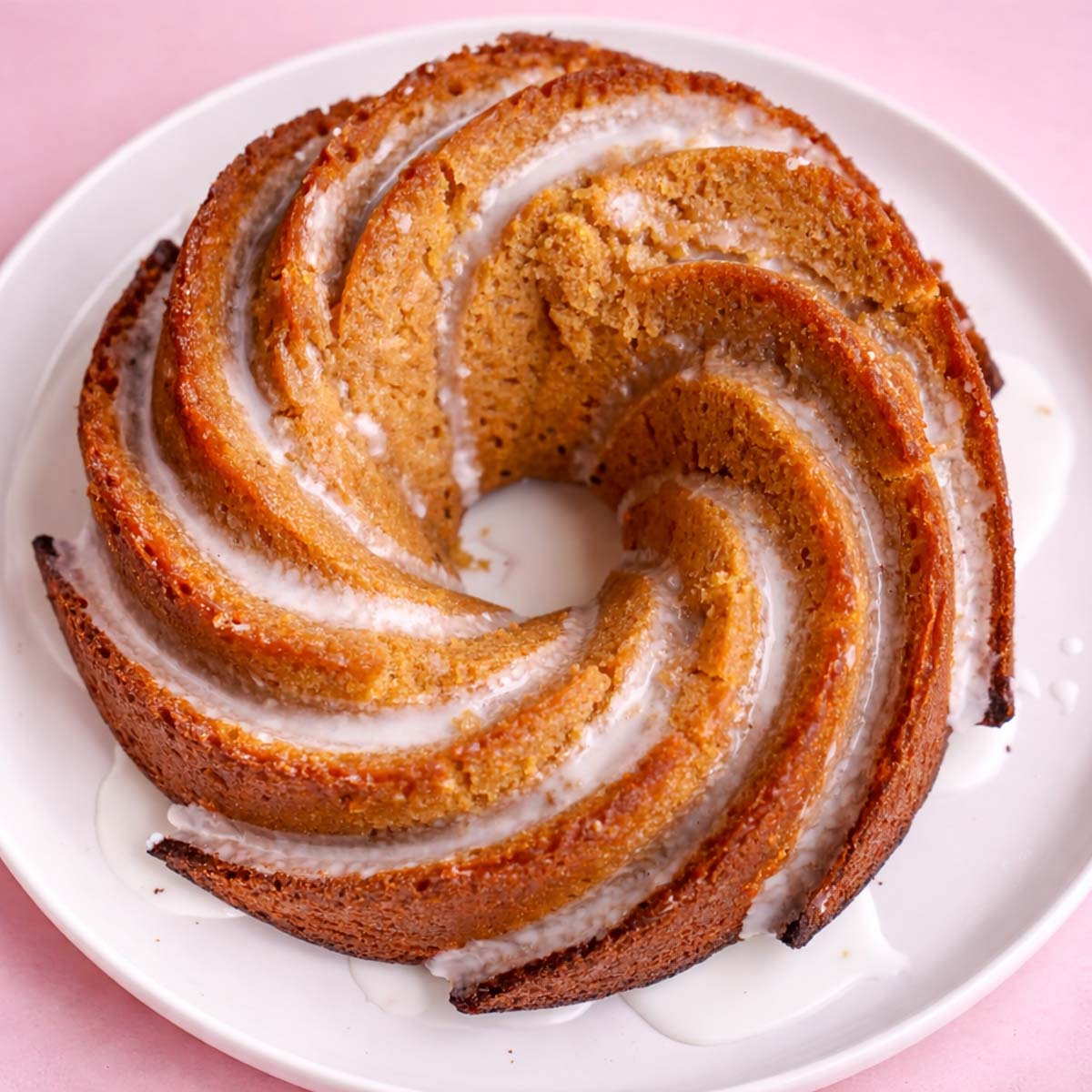 Bishop's cake with a golden spiral shape and light glaze, served on a white plate against a soft pastel pink background