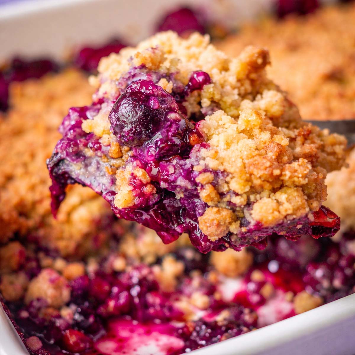 Blueberry Crumble Without Oats with a spoonful of juicy baked blueberries and golden crumb topping lifted from a white baking dish.