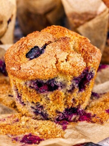 Blueberry muffin with golden sugar crust and juicy blueberries on parchment paper, bakery-style homemade blueberry muffin close-up.