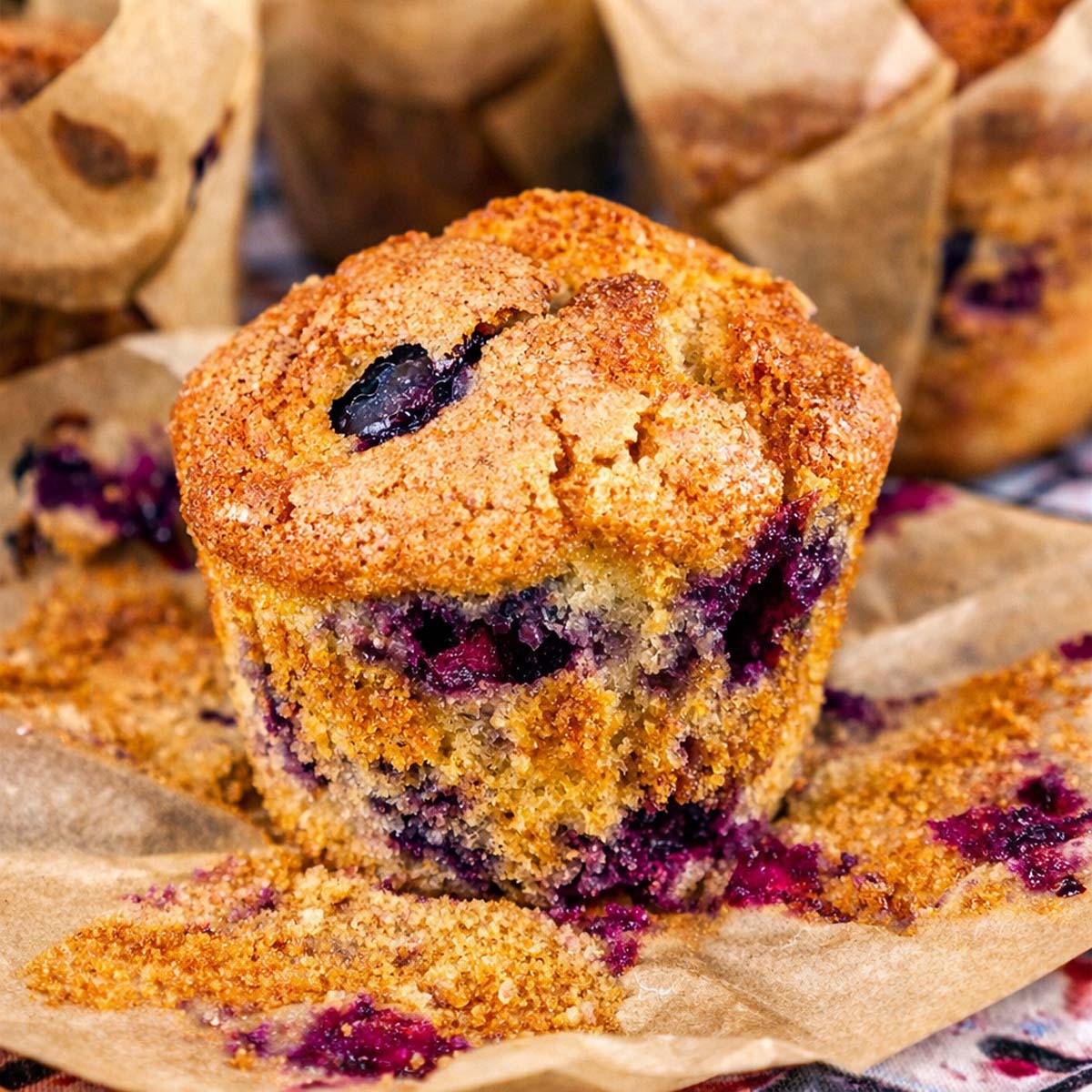 Easy blueberry muffin with golden sugar crust and juicy blueberries on parchment paper, bakery-style homemade blueberry muffin close-up.