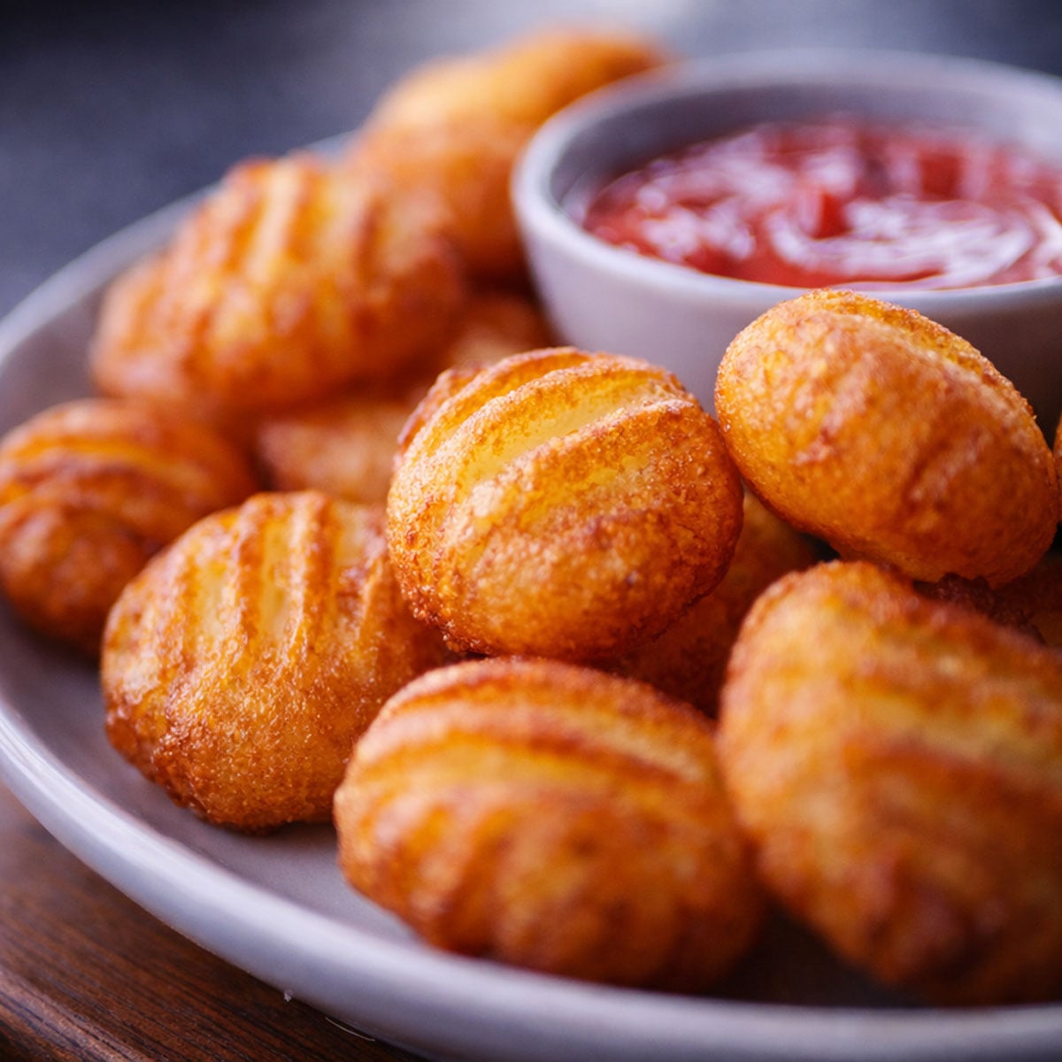 Close-up of bubble potato pillows with a crispy golden crust, served on a plate with ketchup in the background