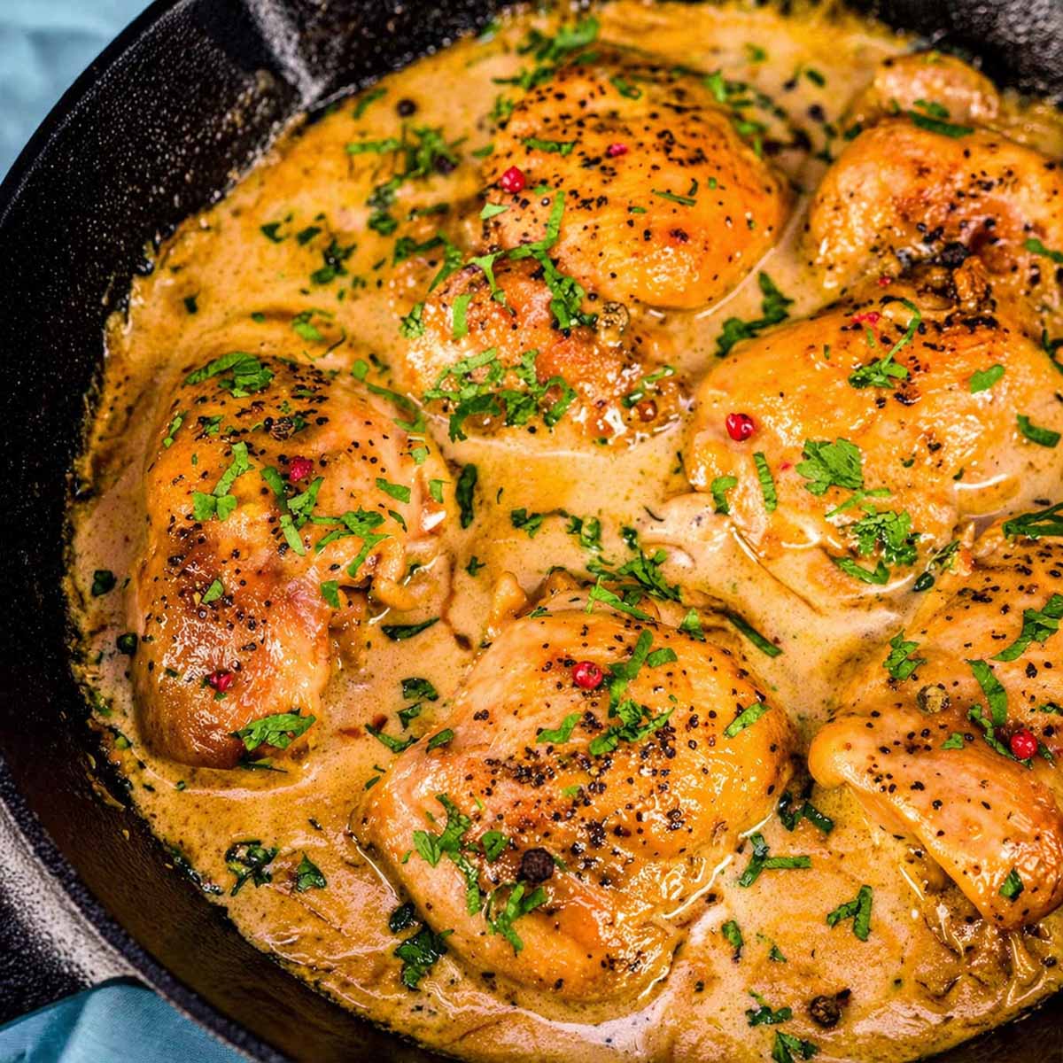 Chicken au Poivre in a cast-iron skillet with golden chicken thighs simmered in creamy peppercorn sauce and garnished with fresh parsley. 
