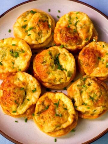Cottage cheese egg bites baked until golden, topped with chopped chives and served on a white plate.
