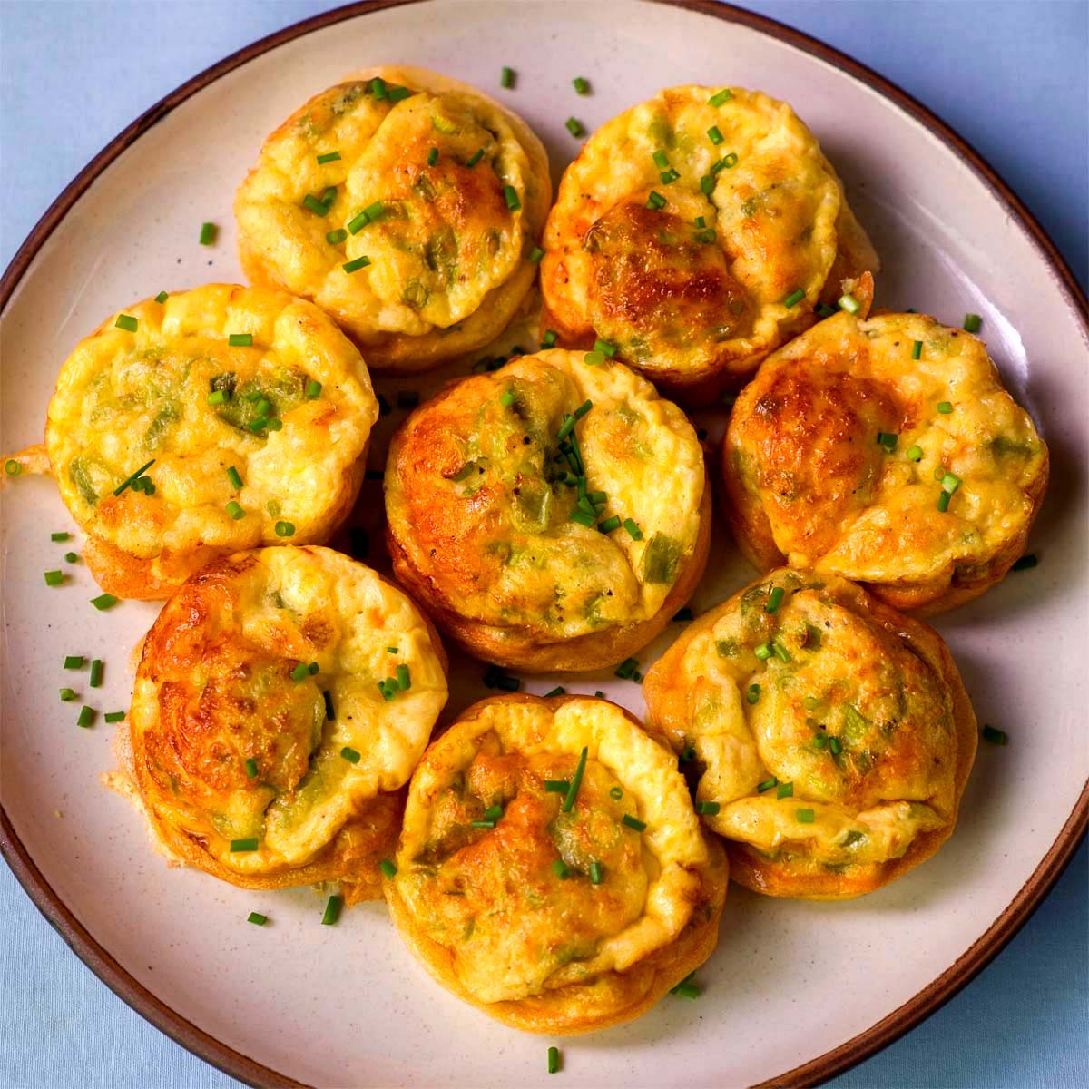 Cottage cheese egg bites baked until golden, topped with chopped chives and served on a white plate.
