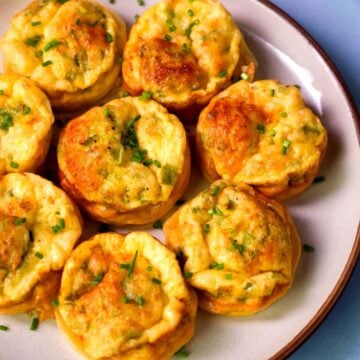Golden cottage cheese egg bites with green onions baked in a muffin tin and served on a white plate.