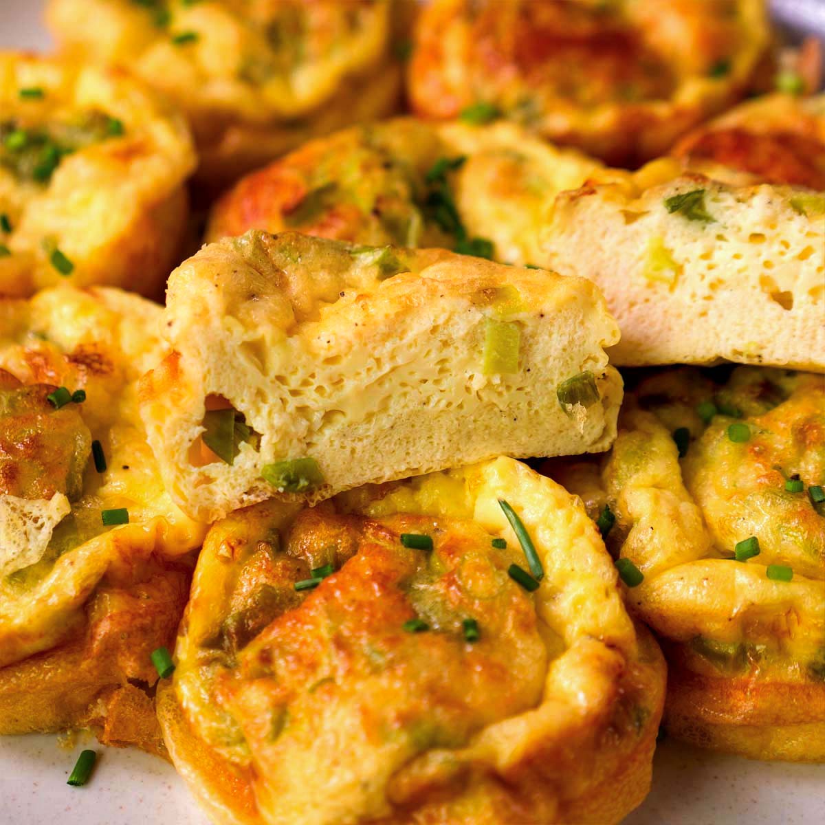 Cottage cheese egg bites cut open to show the fluffy interior with green onions, served warm on a plate.