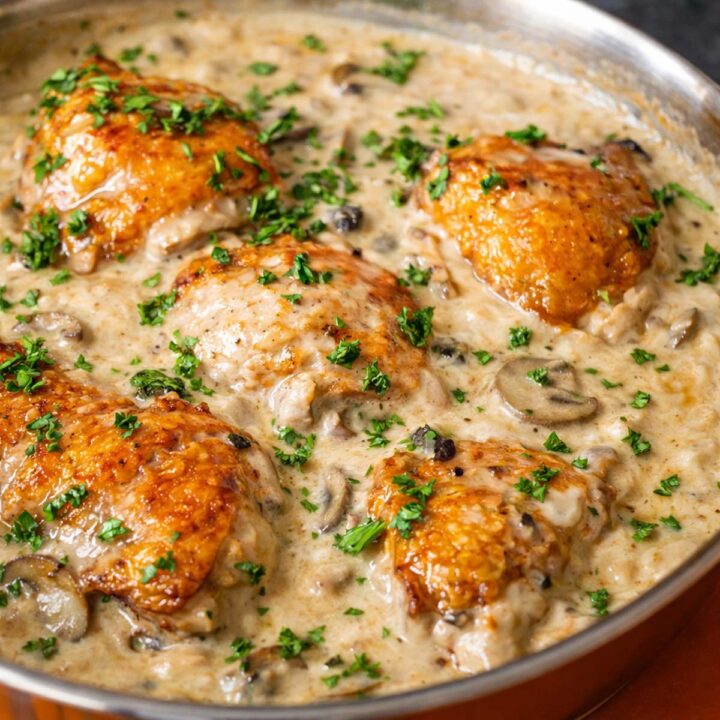 Creamy mushroom chicken thighs in a rich garlic cream sauce with sautéed mushrooms and fresh parsley in a skillet