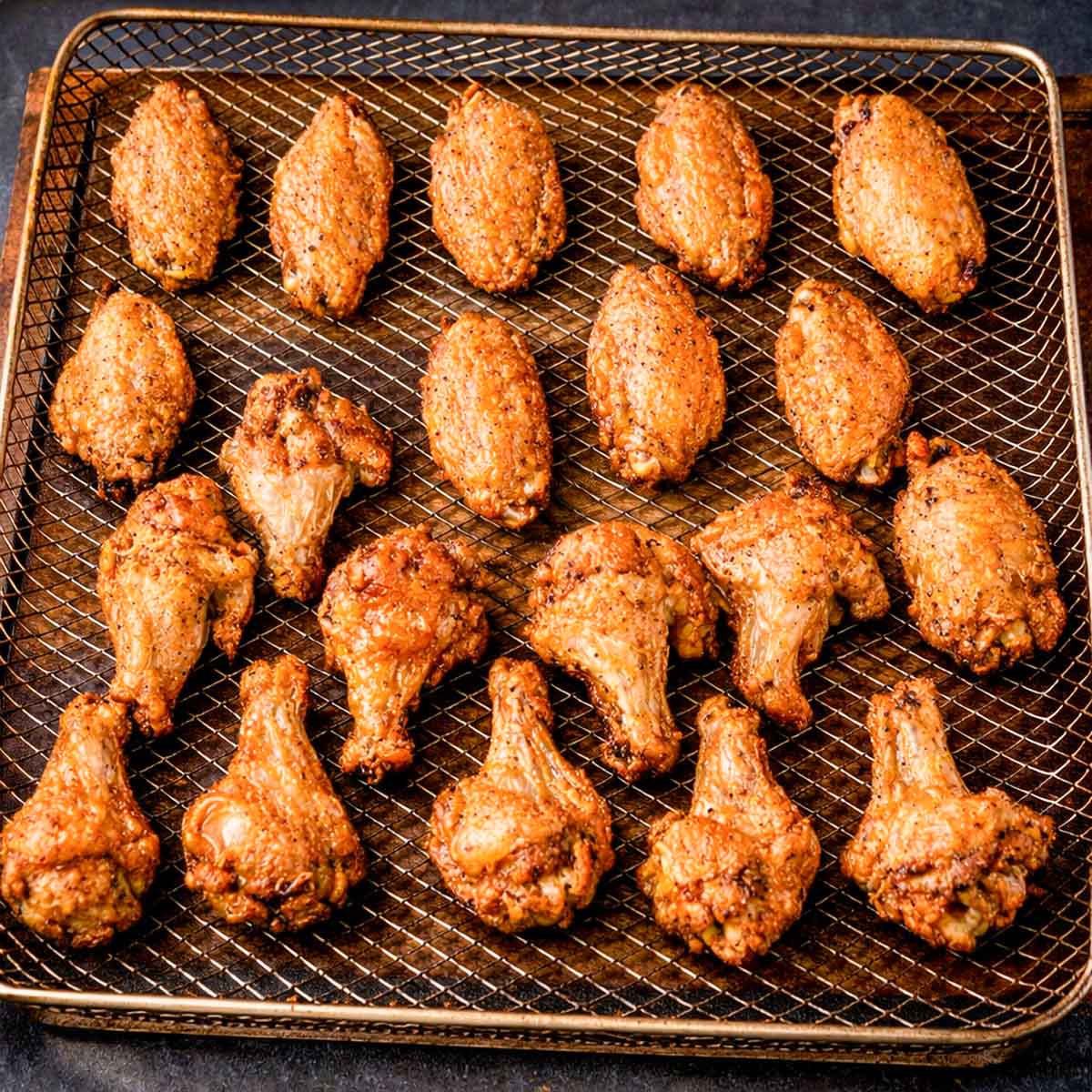 Crispy oven baked chicken wings arranged on a wire rack over a baking tray, showing golden brown skin and evenly roasted wings without frying.