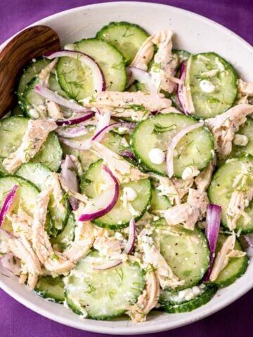 High protein cucumber chicken salad with shredded chicken, sliced cucumber, red onion, feta, and fresh dill in a white bowl