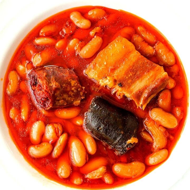Fabada Asturiana Spanish white bean stew in a white bowl with chorizo, morcilla, and a piece of pork belly in a rich broth