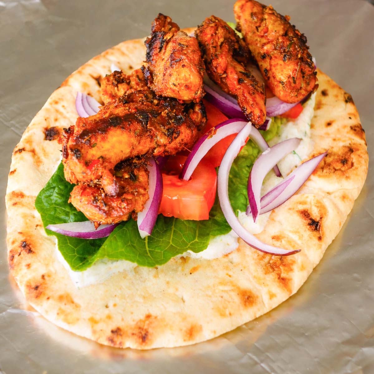 Greek chicken gyros with marinated grilled chicken, lettuce, tomato, and red onion on warm flatbread ready to assemble
