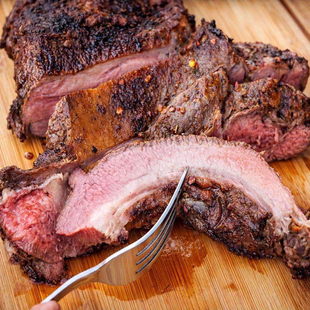 grilled butterflied leg of lamb sliced on a wooden board showing juicy pink center and charred crust