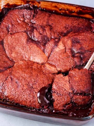 Hot fudge pudding cake in a glass baking dish with a spoon lifting a square, revealing rich chocolate sauce underneath