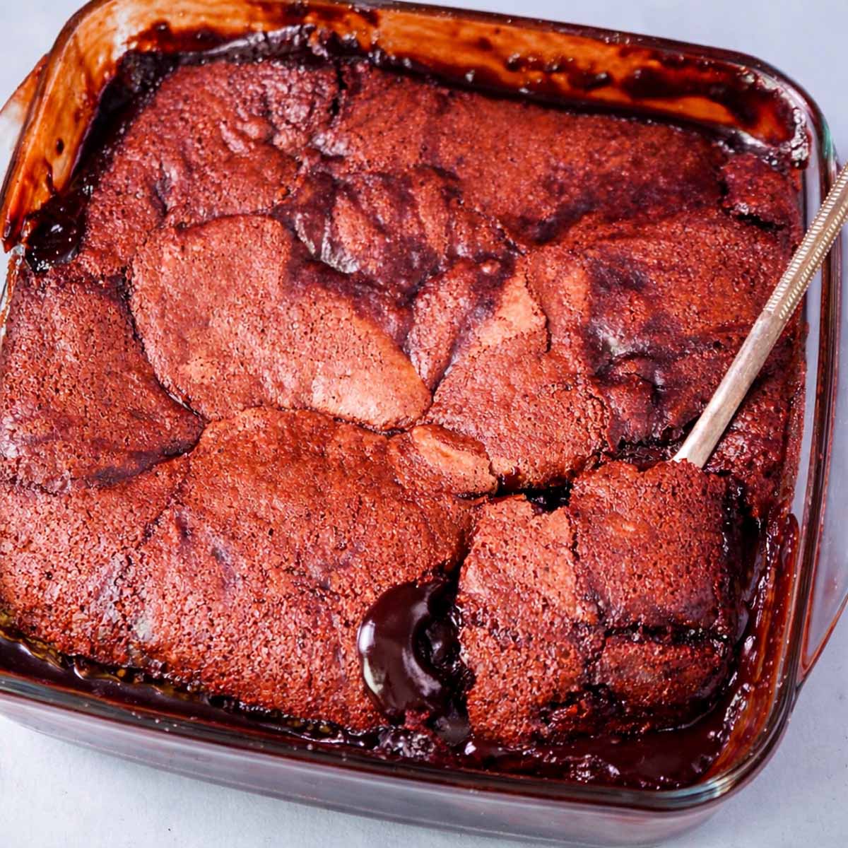 Hot fudge pudding cake in a glass baking dish with a spoon lifting a square, revealing rich chocolate sauce underneath
