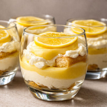 Lemon tiramisu cup with layers of creamy filling, soaked finger biscuits, and lemon curd, topped with a lemon slice in a glass dessert cup
