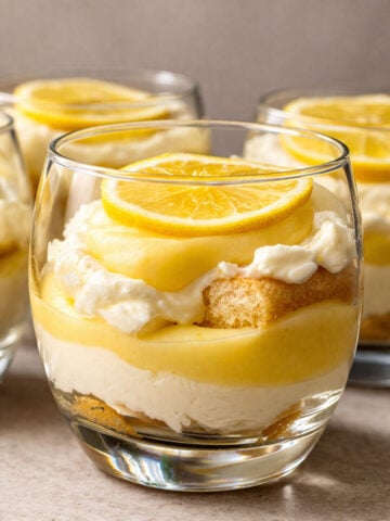 Lemon tiramisu cup with layers of creamy filling, soaked finger biscuits, and lemon curd, topped with a lemon slice in a glass dessert cup