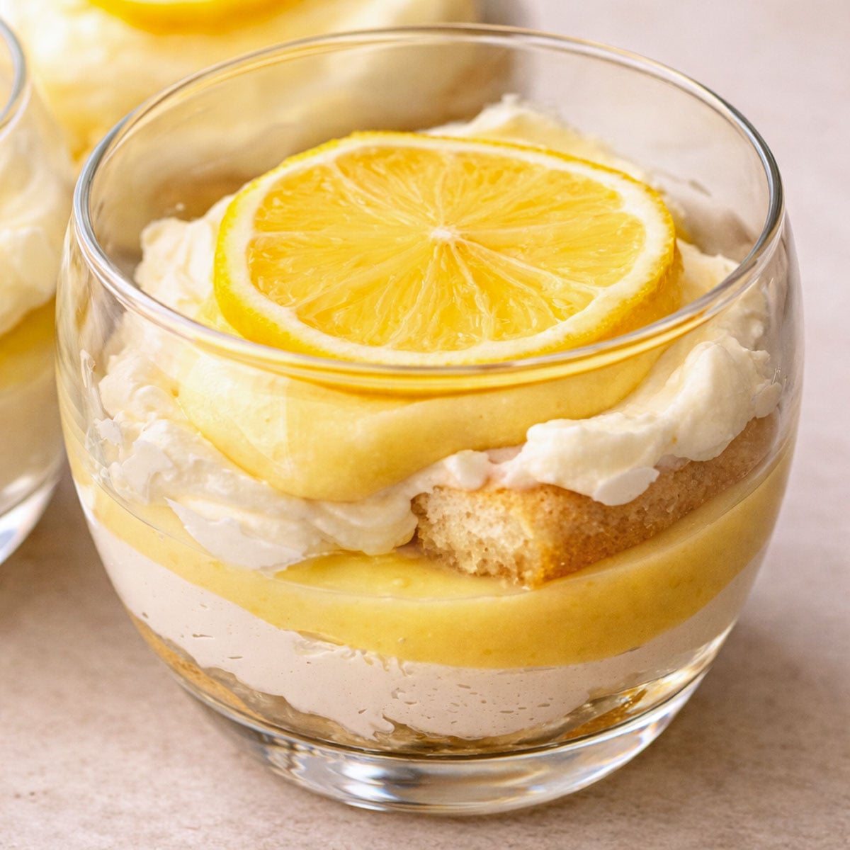 Lemon tiramisu cup with layers of creamy filling, soaked finger biscuits, and lemon curd, topped with a fresh lemon slice in a glass dessert cup