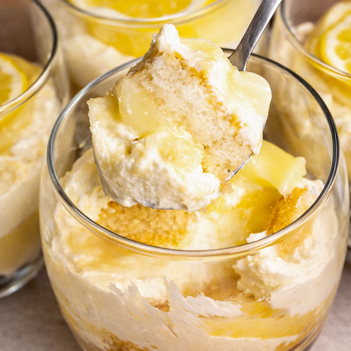 Lemon tiramisu cup with creamy filling and soaked finger biscuits, showing a spoonful of layered dessert with lemon curd in a glass cup