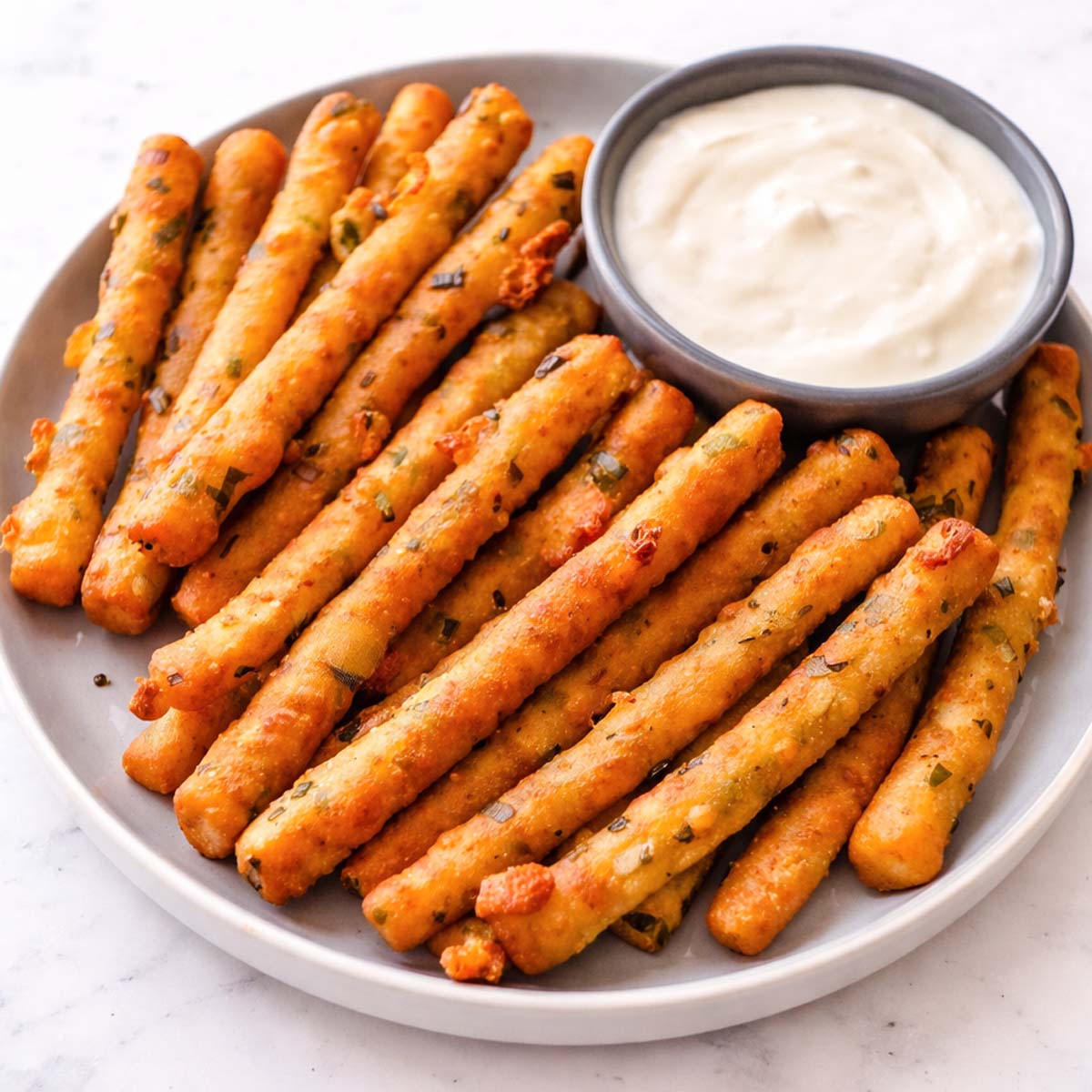 Crispy mashed potato fries on a gray plate with a small bowl of creamy dipping sauce. 