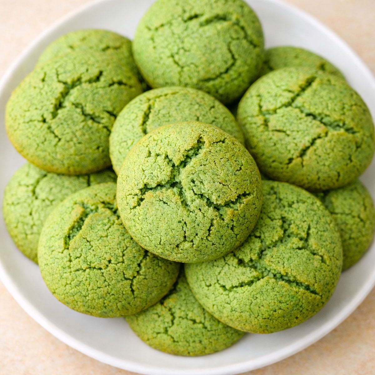 Mint cookies made with fresh mint leaves, stacked on a white plate, with cracked tops and soft green centers baked until lightly golden.