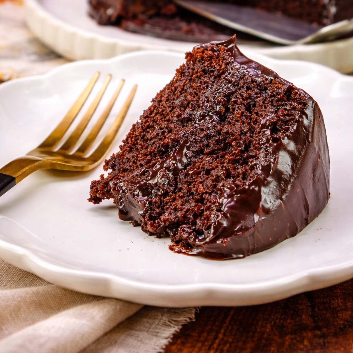 Moist chocolate banana cake slice with glossy ganache on a white plate with a fork, soft tender crumb and rich chocolate texture