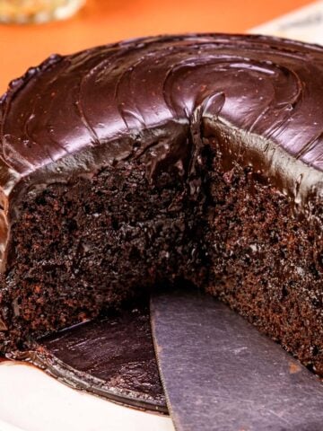 Moist chocolate banana cake with glossy ganache frosting and a slice cut out, soft rich crumb shown on a white plate