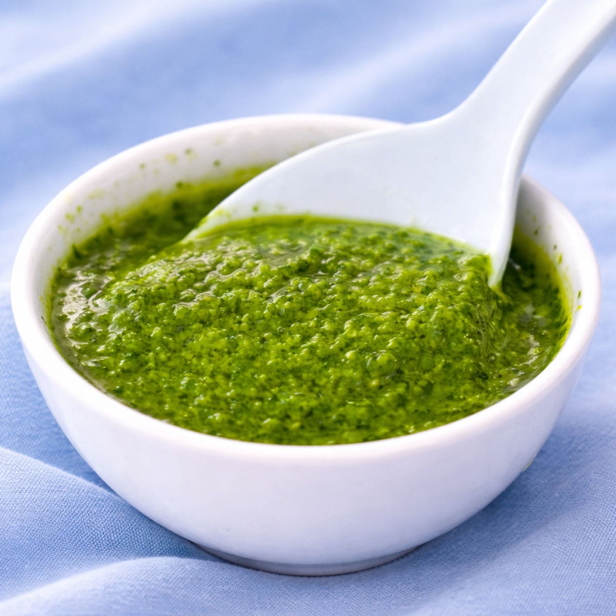 Close-up of mojo verde sauce in a small white bowl with a spoon, showing the bright green, garlicky herb sauce. 