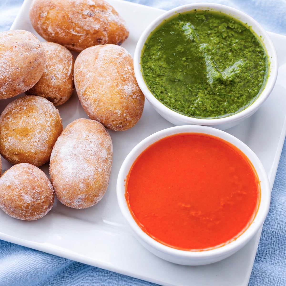 Mojo verde and mojo rojo sauce in small bowls on a white platter with papas arrugadas (wrinkled potatoes). 