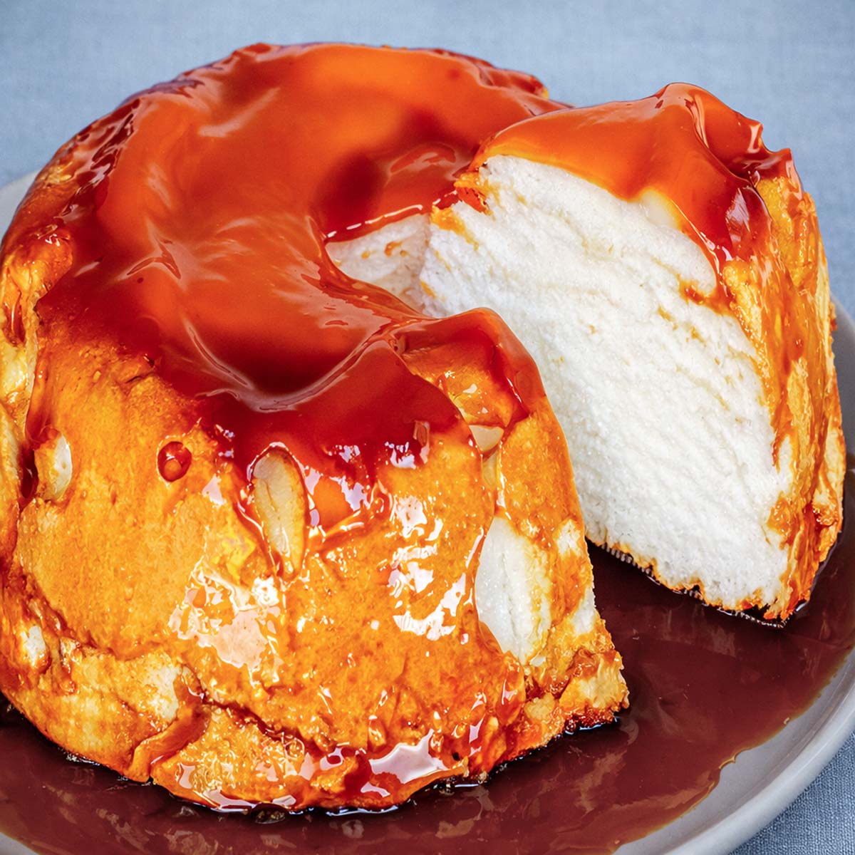 Slice of Molotof Cake (Portuguese meringue cake) lifted to show the airy white meringue inside, with caramel sauce dripping over the top and plate. 