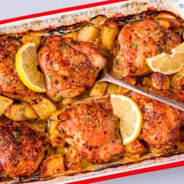 One pan Greek lemon chicken and potatoes with crispy chicken thighs, roasted potatoes, and fresh lemon slices in a baking dish
