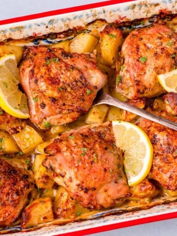 One pan Greek lemon chicken and potatoes with crispy chicken thighs, roasted potatoes, and fresh lemon slices in a baking dish