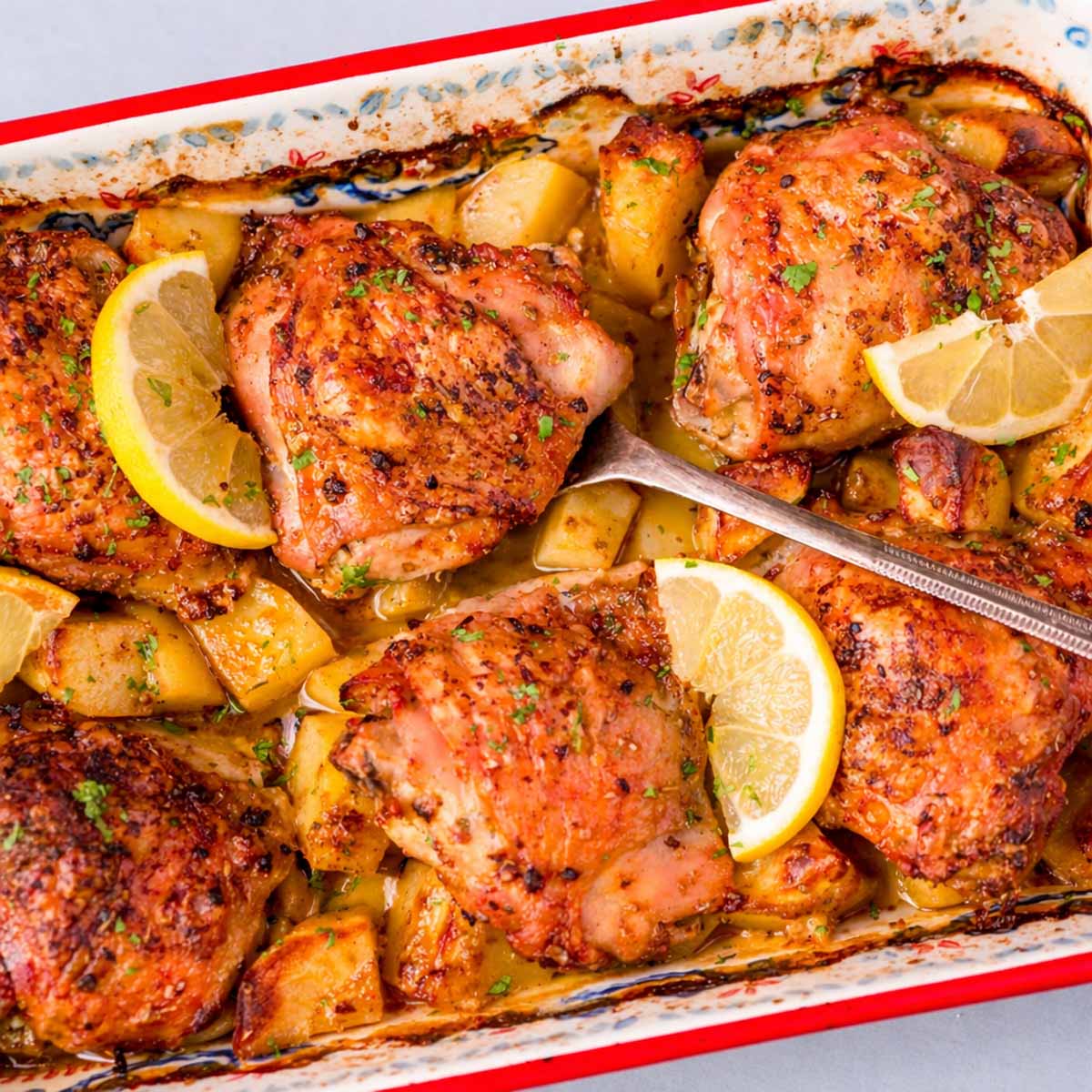 One pan Greek lemon chicken and potatoes with crispy chicken thighs, roasted potatoes, and fresh lemon slices in a baking dish
