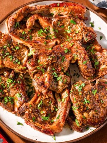 Pan seared lamb chops with garlic sauce and fresh parsley served on a plate.