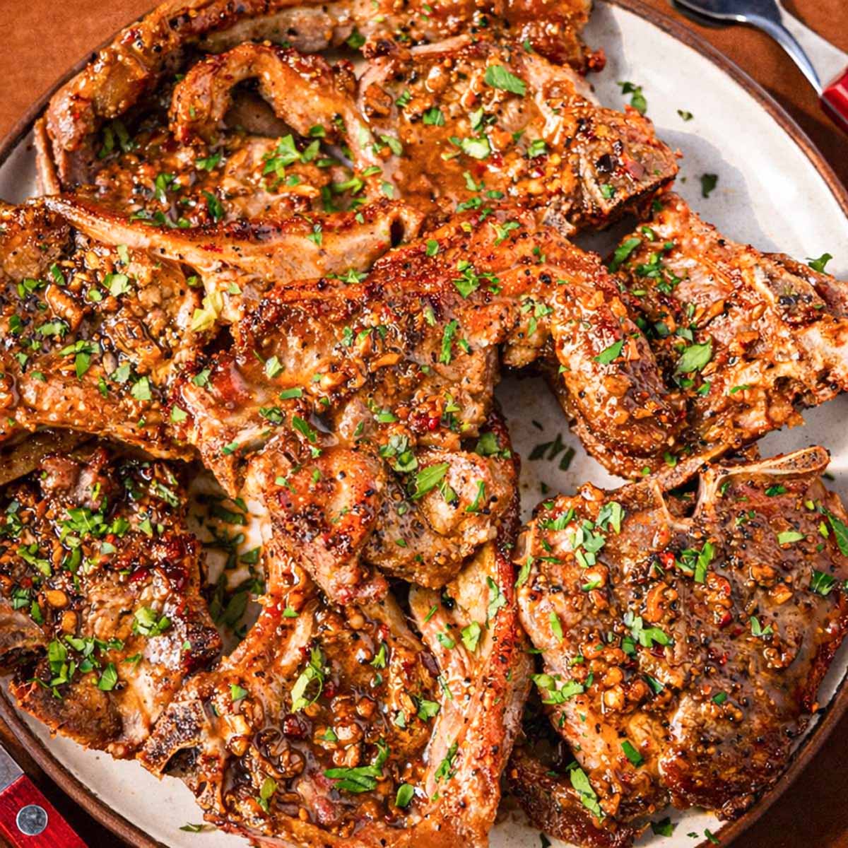 Pan seared lamb chops with garlic butter sauce and parsley served on a platter.