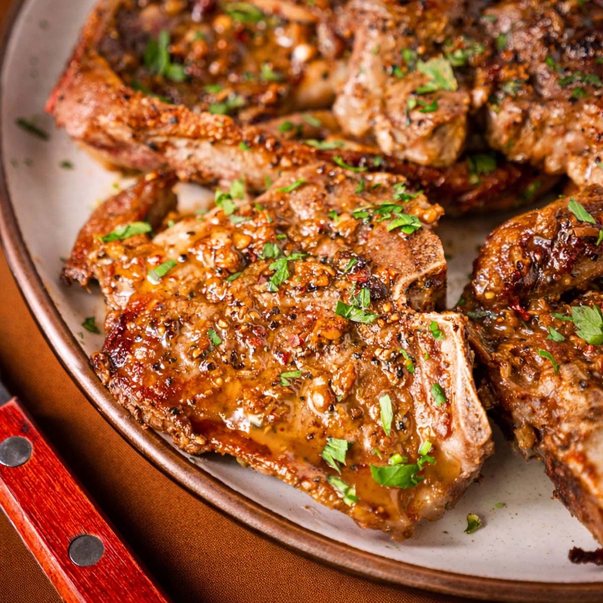 Close-up of pan seared lamb chops with garlic sauce and chopped parsley on a plate.