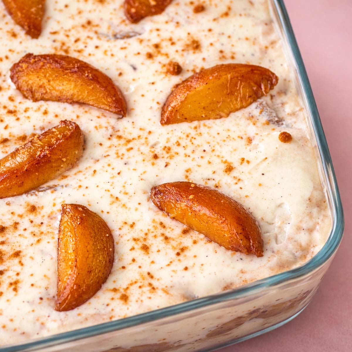 Peach cobbler pudding in a glass baking dish topped with whipped cream, cinnamon sprinkles, and peach slices.